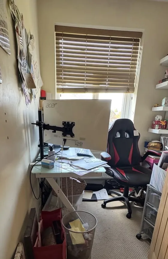A small home office before: the desk pushed against the wall and covered in papers, with bags, a full bin and boxes on the floor